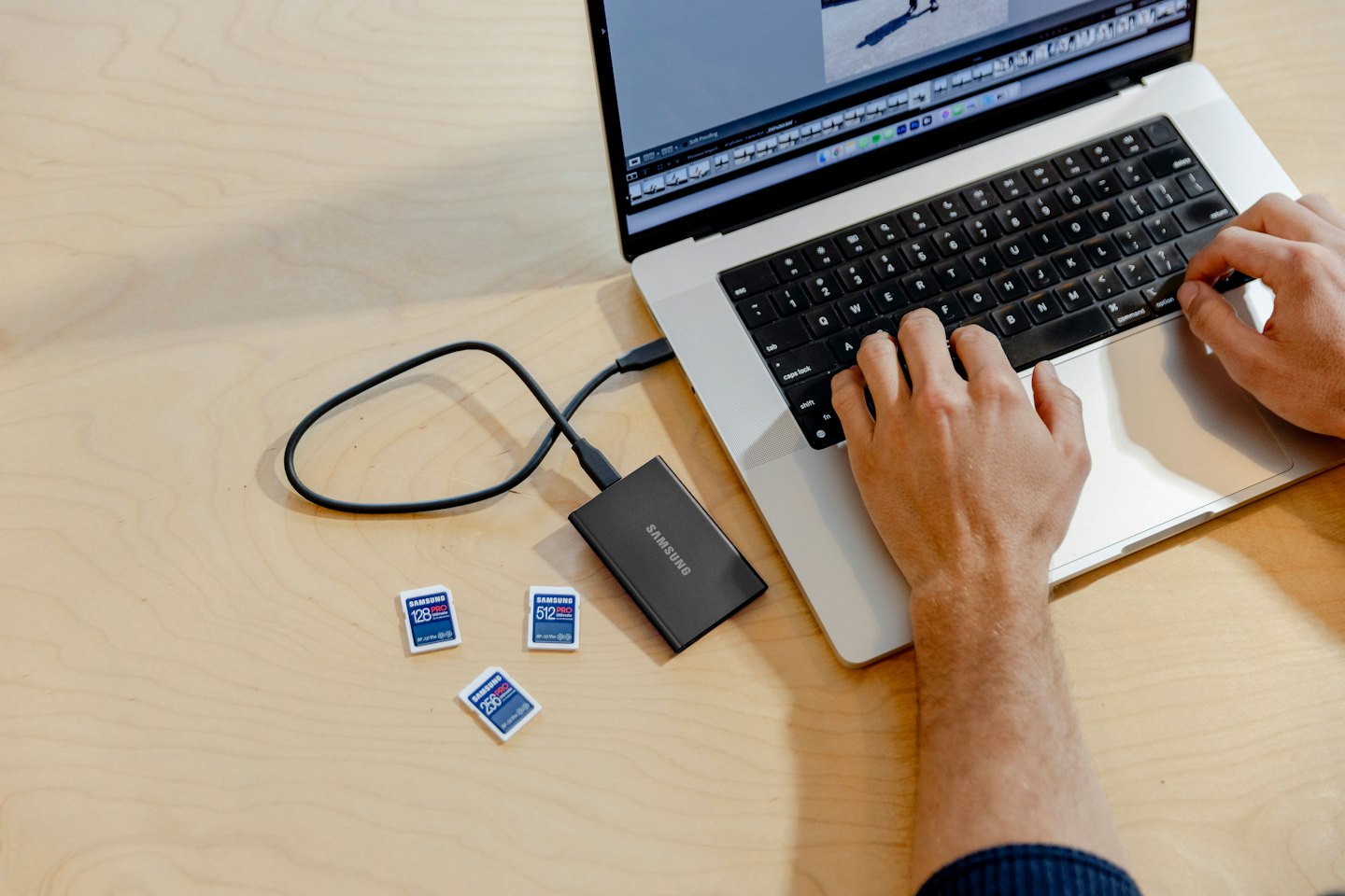 Mani che digitano su una tastiera di laptop con un hard disk esterno e schede microSD.